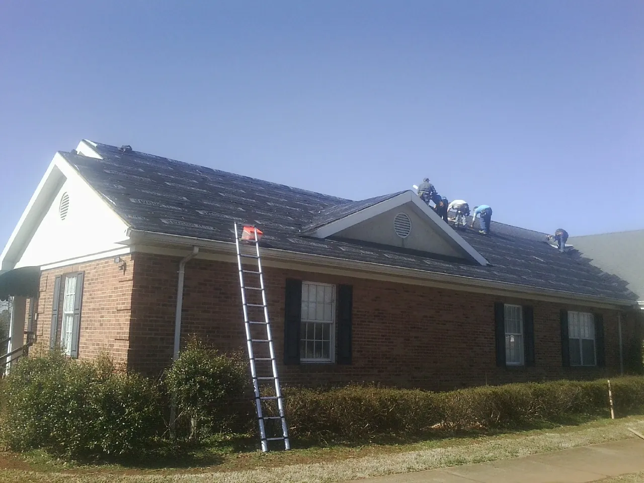 Crew tearing shingles off a brick ranch roof with a ladder set — Emergency Roof Repair work by our crew in Hanover